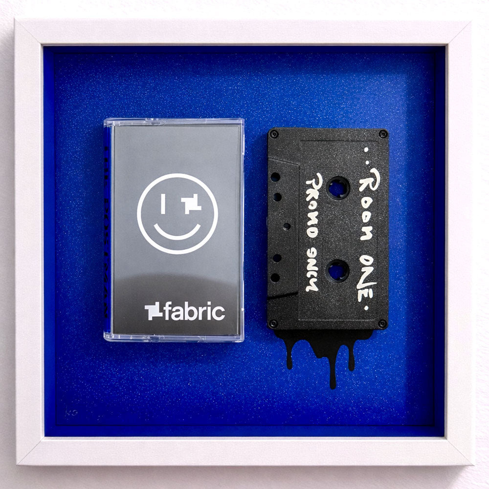 Framed mixed-media cassette artwork featuring a Fabric inspired tape case and a hand-written “Room One – Promo Only” cassette with paint drips, set against a deep blue speckled background. The Postman